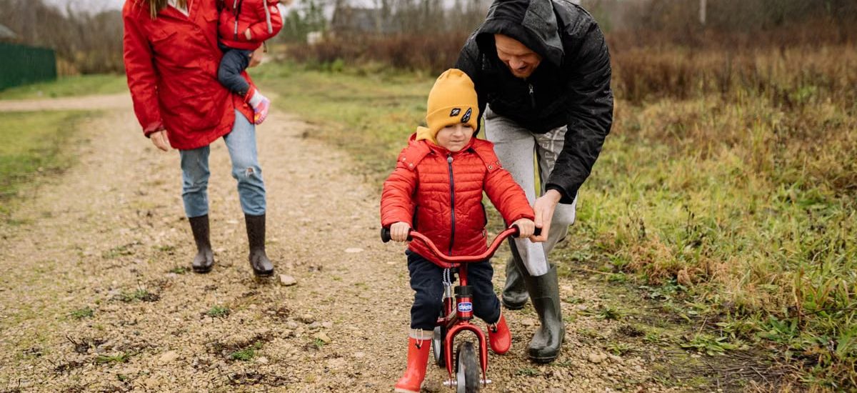 Happy family walking outdoors in fall, teaching child to ride bike.