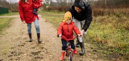 Happy family walking outdoors in fall, teaching child to ride bike.