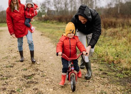 Happy family walking outdoors in fall, teaching child to ride bike.